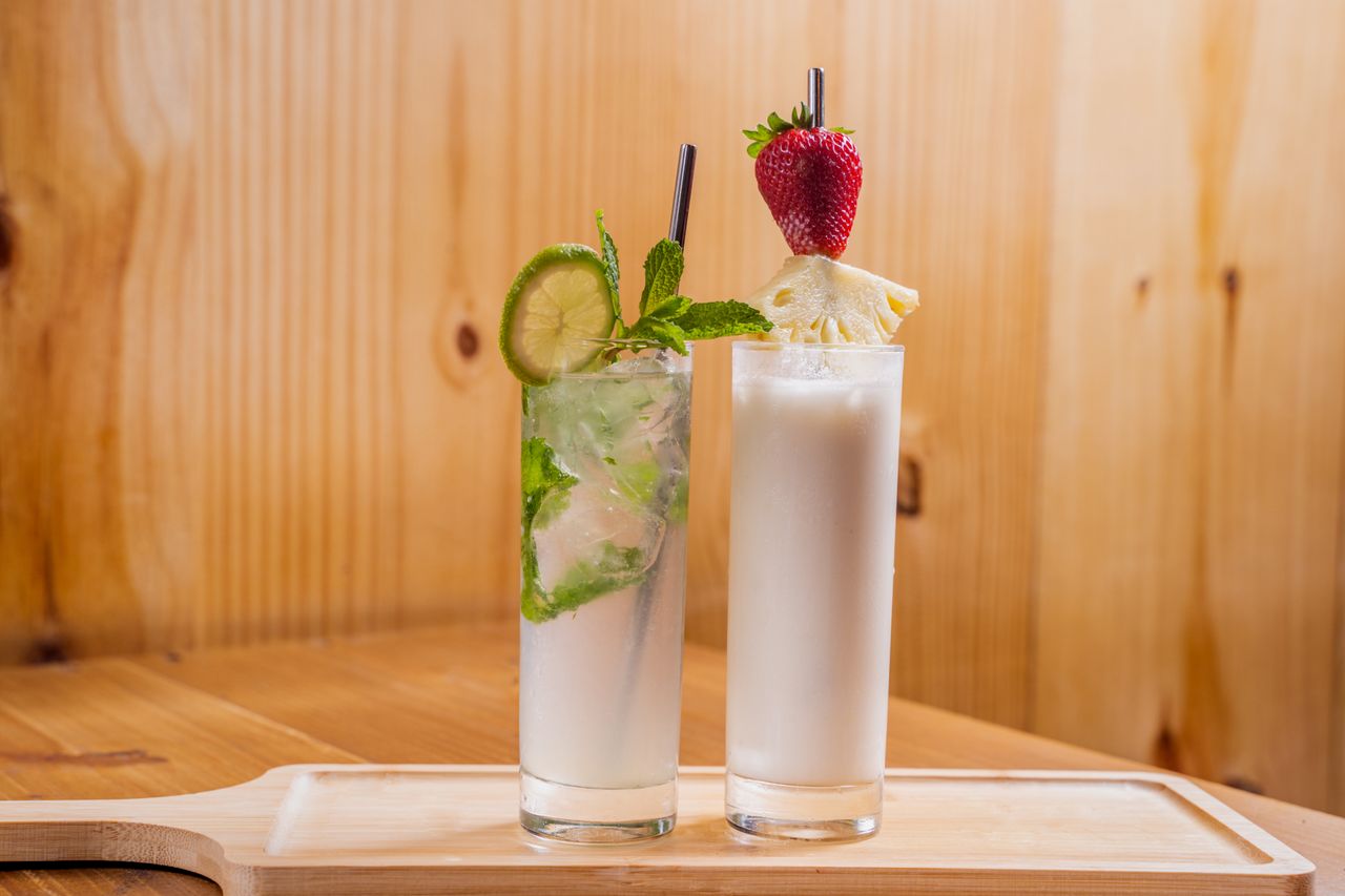 services-04 Two refreshing cocktails with lime, mint, strawberry, and pineapple garnishes on a wooden surface.