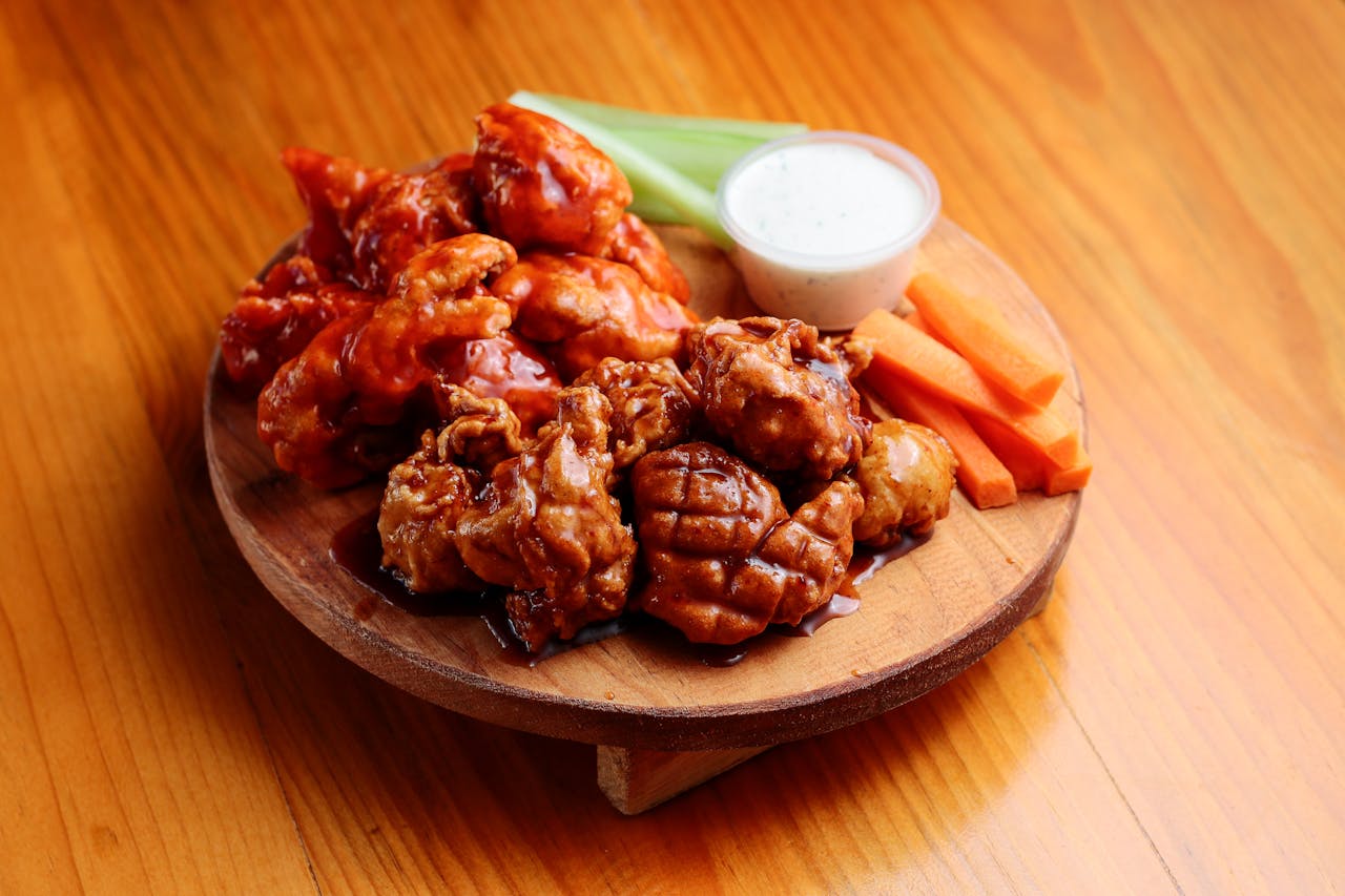 hero-img-01 Tasty chicken wings served with vegetables and sauce on a wooden plate.