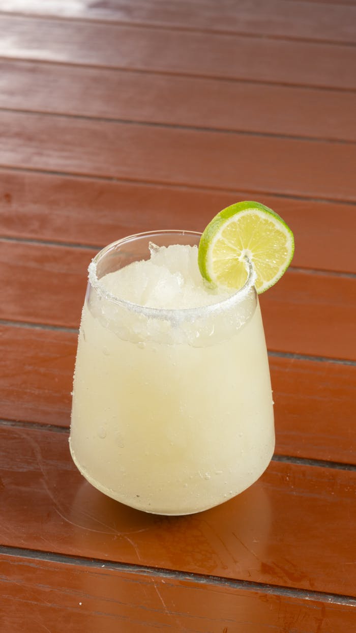 gallery-2 A chilled margarita topped with lime on a wooden table, perfect for summer vibes.