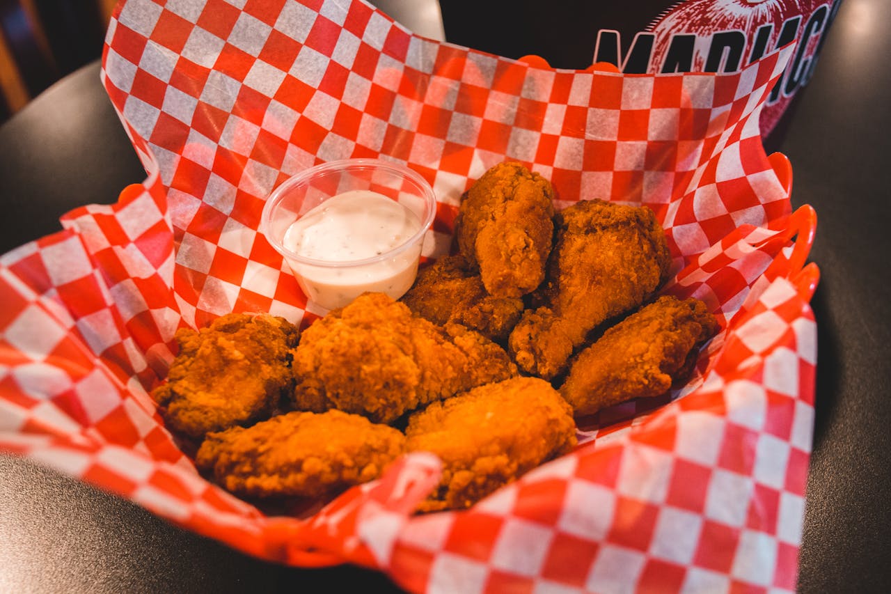 hero-img-02 Tasty crispy fried chicken wings served with ranch dipping sauce on a checkered paper.